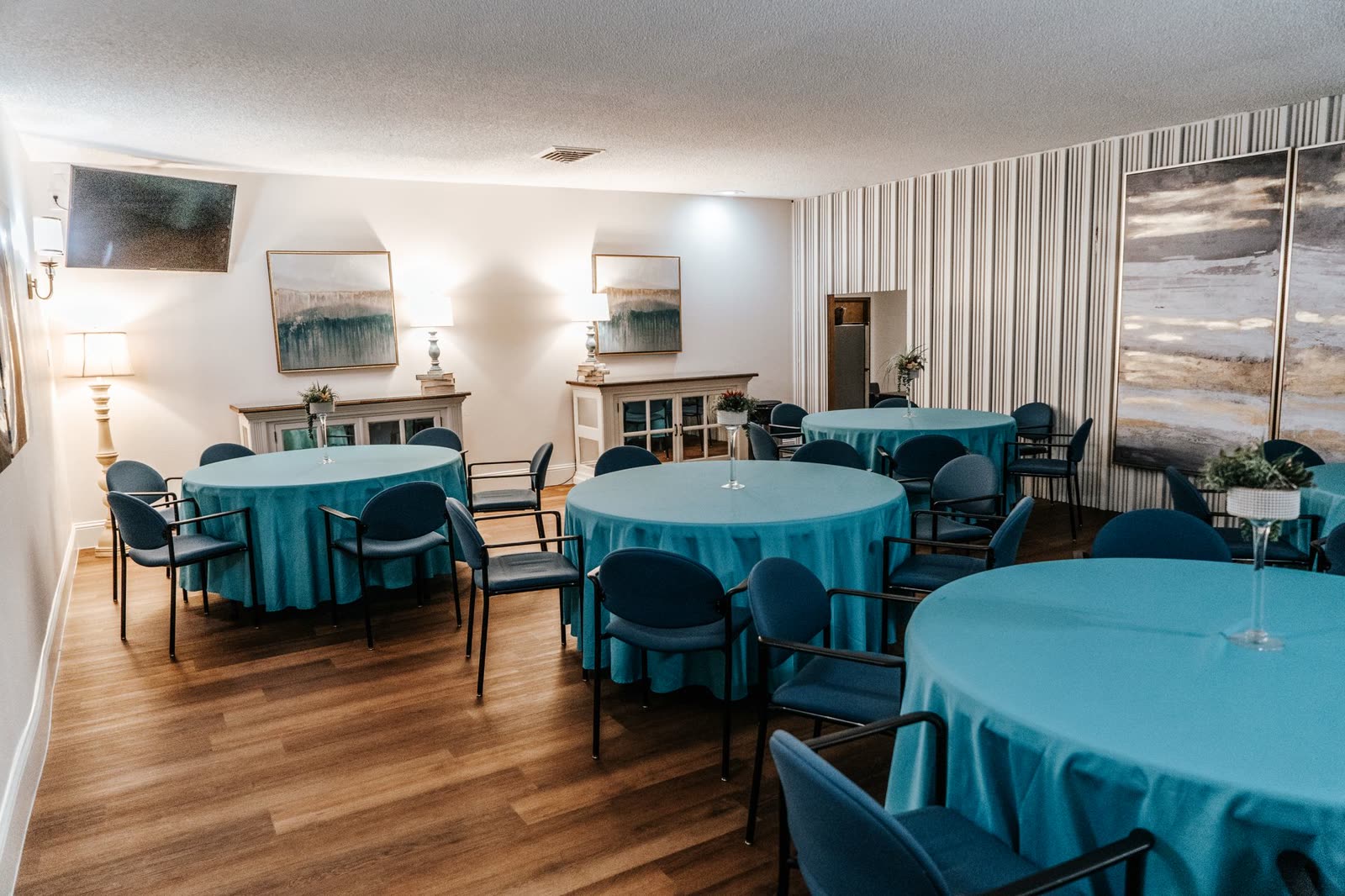 The event room, set with round tables in teal linen and blue chairs for a reception